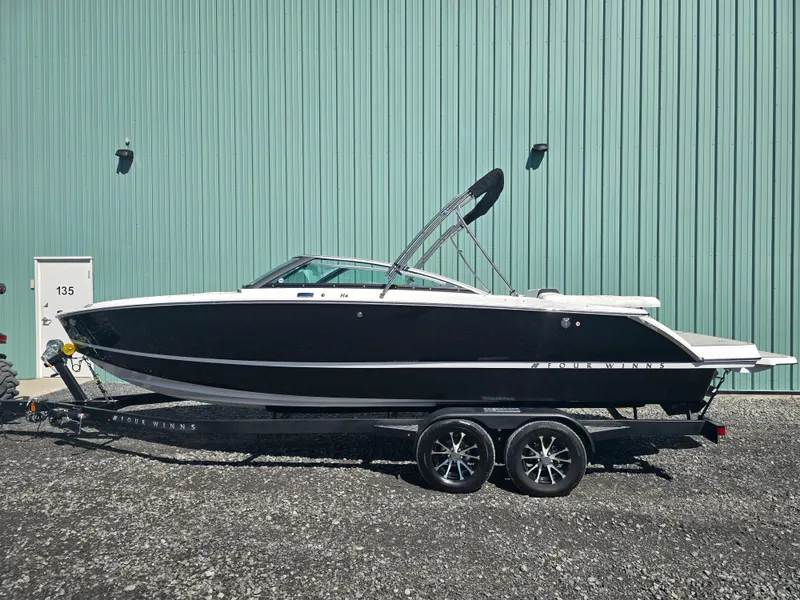The Image of 2025 Four Winns H4 boat on trailer, parked by a green building. - 1