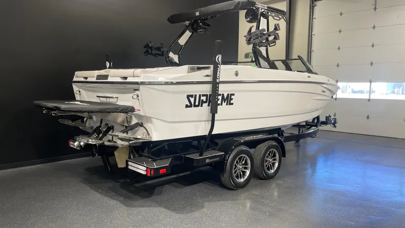 Slide: The Image of 2024 Supreme S220 boat in showroom, white exterior, on a trailer. - 2