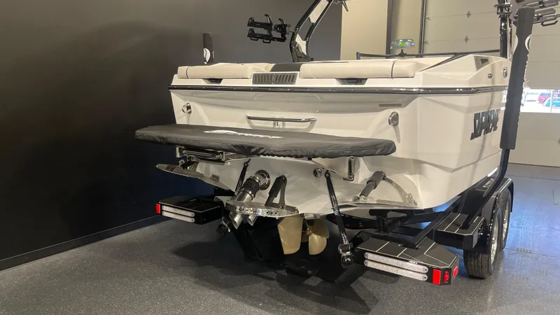 Slide: The Image of 2024 Supreme S220 boat, rear view in showroom, showcasing sleek design and dual-axle trailer. - 3