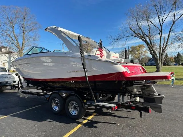 Slide: The Image of 2025 Regal LS9 Surf boat on trailer, parked outdoors, with American flag. - 4