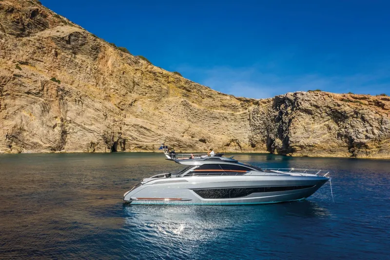 Slide: The Image of Luxury 2024 Riva 66' Ribelle yacht cruising near rocky cliffs under clear blue sky. - 6