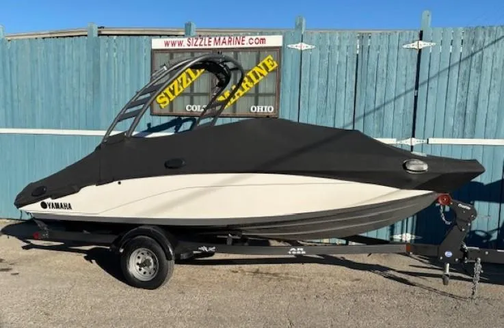 Slide: The Image of 2020 Yamaha Boats 195S covered on trailer, parked by blue fence. - 32