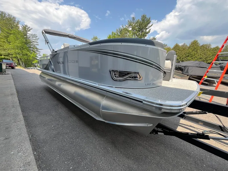 Slide: The Image of 2025 Avalon LSZ Versatile Rear Bench pontoon boat on trailer, parked outdoors. - 3