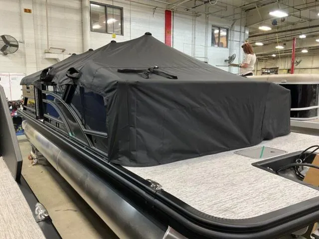 Slide: The Image of 2025 Bennington 23 SSB pontoon boat with black cover in a warehouse setting. - 17
