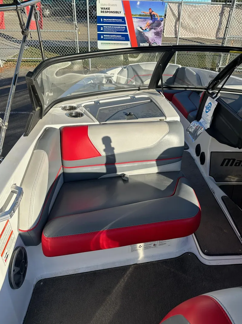 Slide: The Image of 2019 Malibu TXi Mo boat interior with red and gray seating, cup holders, and safety signage. - 14