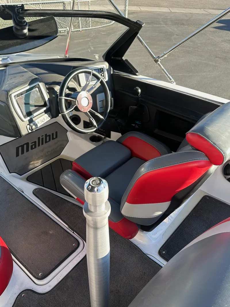 Slide: The Image of 2019 Malibu TXi Mo boat interior with red and gray seating, steering wheel, and dashboard. - 15
