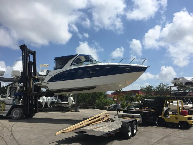Slide: The Image of 2015 Bayliner 335 Cruiser being lifted by forklift under a clear blue sky. - 3