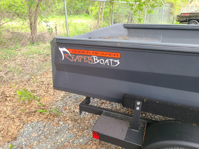 Slide: The Image of 2024 Reaper Boats 653 trailer, black, parked outdoors near a fence. - 2