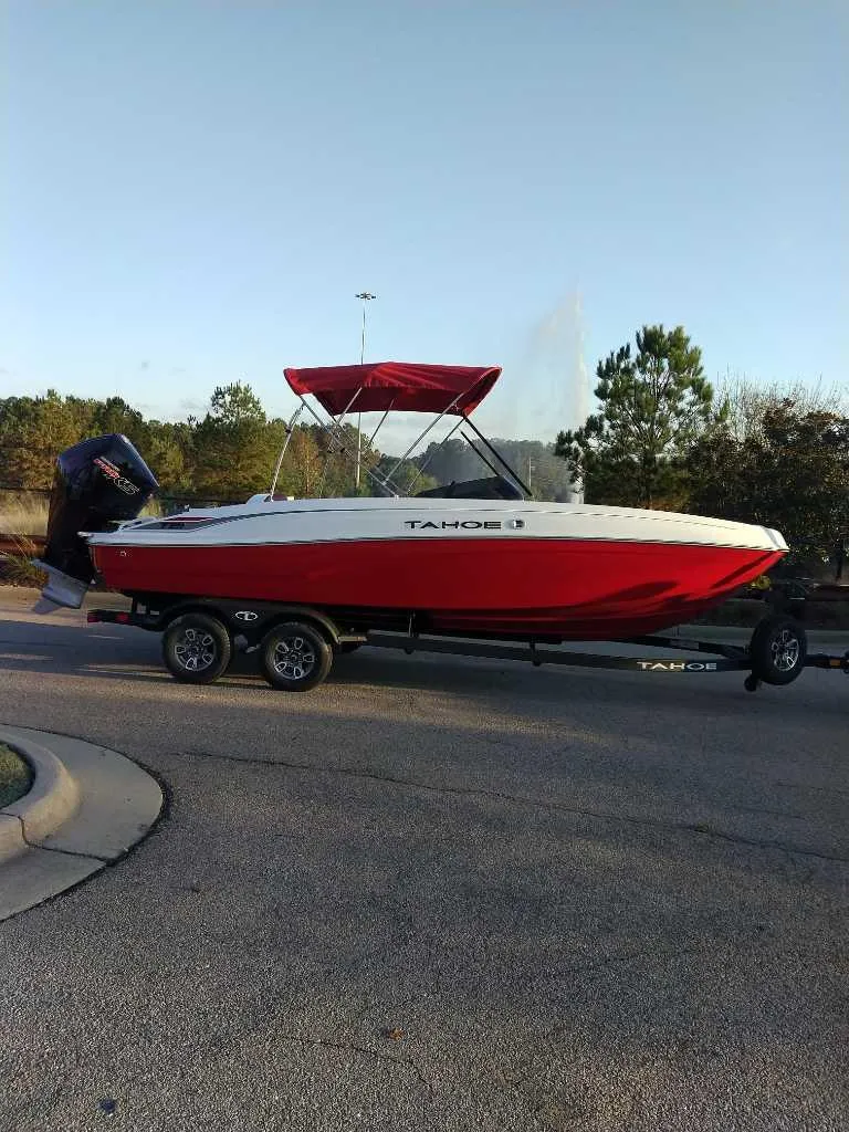 The Image of 2025 Tahoe T21 boat with red and white design on a trailer, parked outdoors. - 0