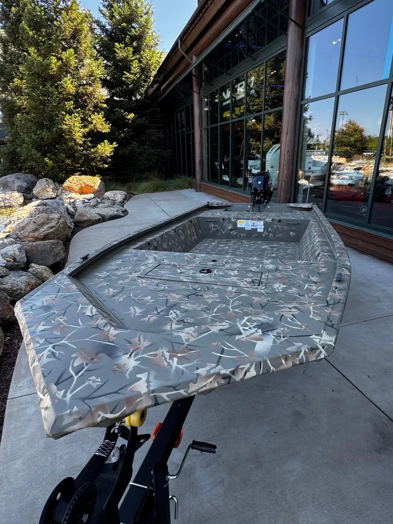 Slide: The Image of 2025 Tracker Grizzly 1648 Jon boat with camouflage design, displayed outdoors near a building. - 3