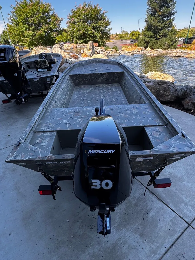 Slide: The Image of 2025 Tracker Grizzly 1648 Jon boat with Mercury 30 engine, parked near a pond. - 4