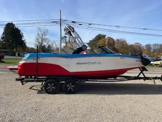 The Image of 2023 MasterCraft NXT22 boat on trailer, red and white design, parked outdoors. - 0