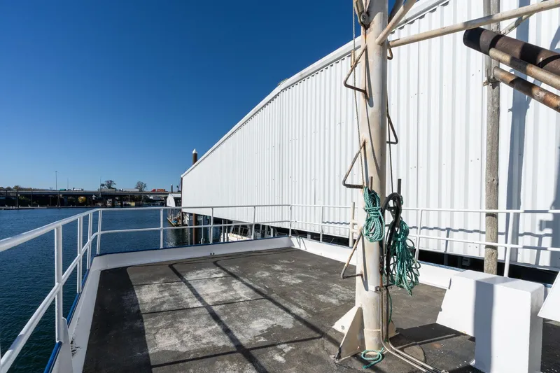 Slide: The Image of 1980 Commercial Troller deck with ropes, docked by a white warehouse, under clear blue sky. - 34