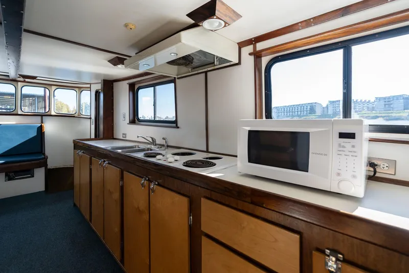 Slide: The Image of 1980 Commercial Troller interior kitchen with microwave, stove, and sink, featuring wood cabinetry and windows. - 9