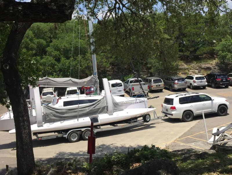 Slide: The Image of Corsair 970 sailboat on trailer in parking lot, surrounded by trees and vehicles, 2025 model. - 1