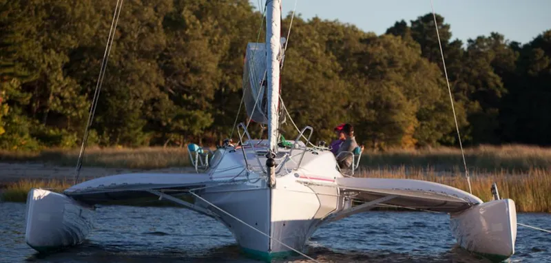 Slide: The Image of Corsair 970 trimaran sailing near a forested shoreline, 2025 model. - 11