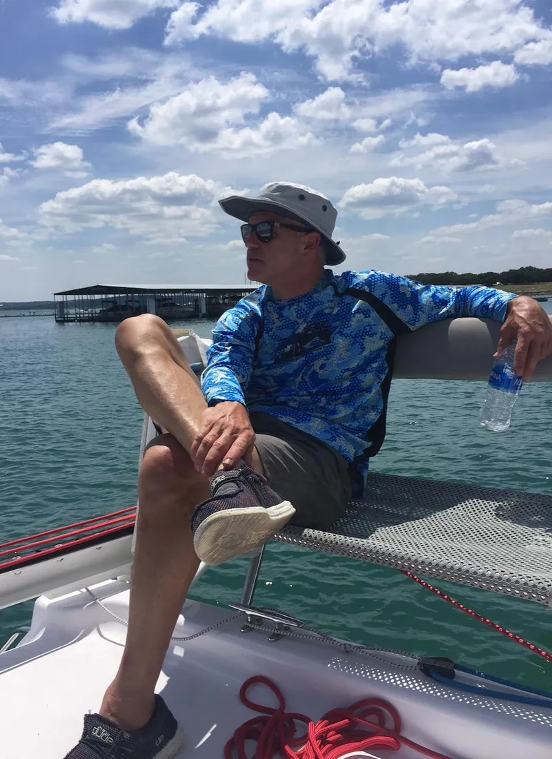 Slide: The Image of Man relaxing on a 2025 Corsair 970 Sport sailboat under a sunny sky. - 13