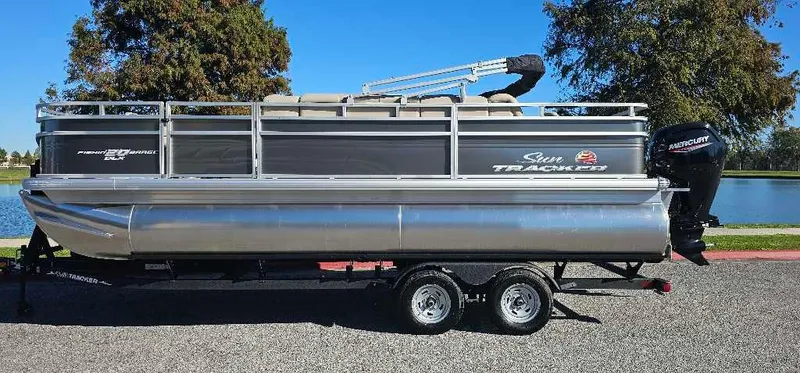 The Image of 2025 Sun Tracker Fishin' Barge 20 DLX pontoon boat on trailer, parked outdoors. - 0