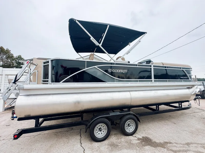 Slide: The Image of 2024 Godfrey Sweetwater 22' Rear Fish & Cruise Tritoon on trailer, black exterior, canopy open. - 2