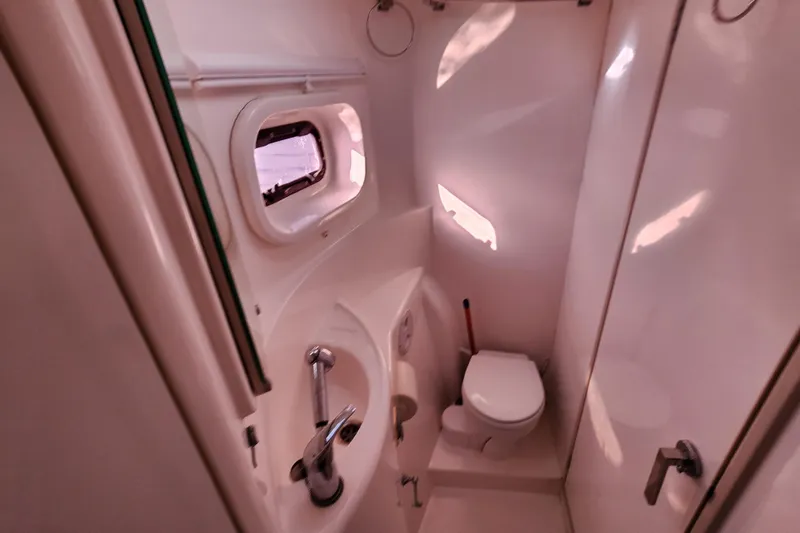 Slide: The Image of Compact bathroom in a 2015 Leopard 44 yacht, featuring a toilet, sink, and porthole window. - 185