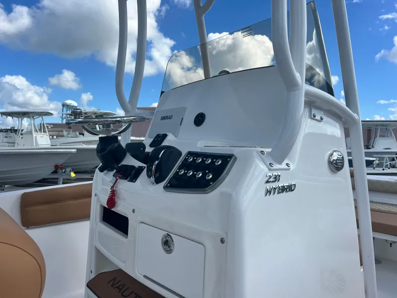 Slide: The Image of 2025 NauticStar 231 Hybrid boat console with controls and seating, under a blue sky. - 9