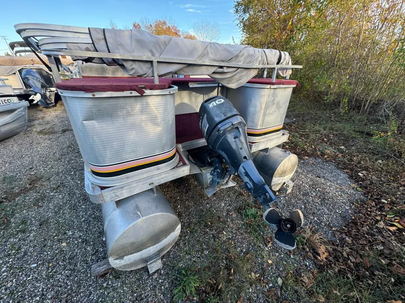 Slide: The Image of 1989 Godfrey Executive Cruiser pontoon boat with outboard motor, parked on gravel. - 3