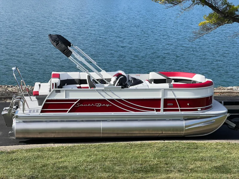 The Image of 2025 South Bay S 220 CR2 pontoon boat by a lake, featuring red and white design. - 0