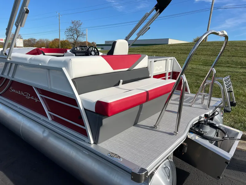 Slide: The Image of 2025 South Bay S 220 CR2 pontoon boat with red and white seating, docked outdoors. - 6