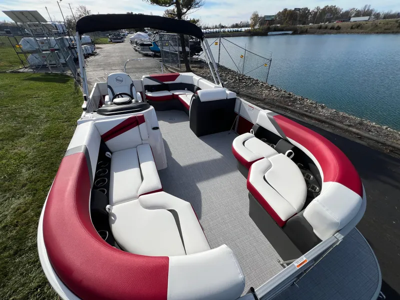 Slide: The Image of 2025 South Bay S 220 CR2 pontoon boat with red and white seating, docked by a lake. - 7