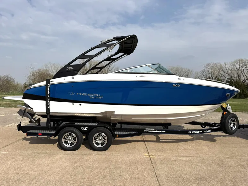 Slide: The Image of 2025 Regal LS4 Surf boat on trailer, blue and white design, parked outdoors. - 11