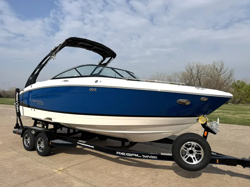 Slide: The Image of 2025 Regal LS4 Surf boat on trailer, blue and white design, parked outdoors. - 12