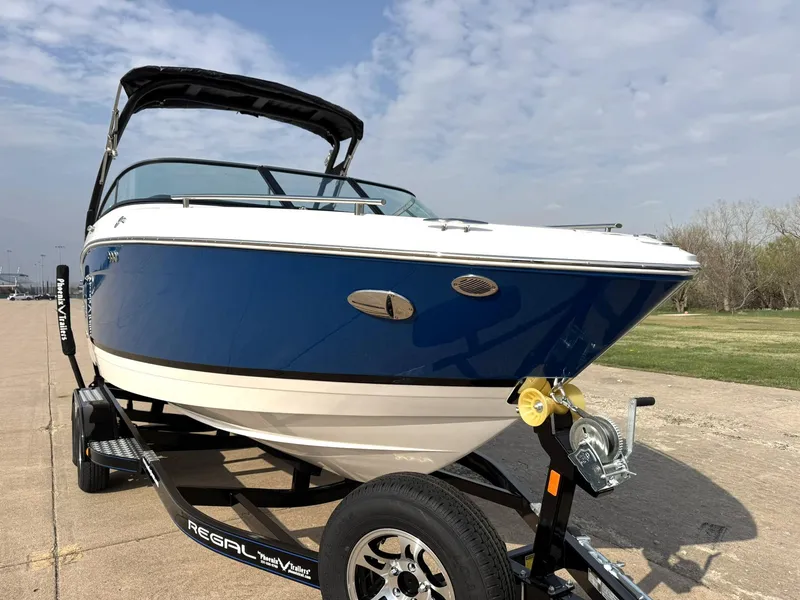 Slide: The Image of 2025 Regal LS4 Surf boat on trailer, blue and white design, parked outdoors. - 13