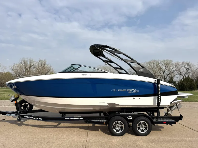 Slide: The Image of 2025 Regal LS4 Surf boat on trailer, blue and white design, parked outdoors. - 2
