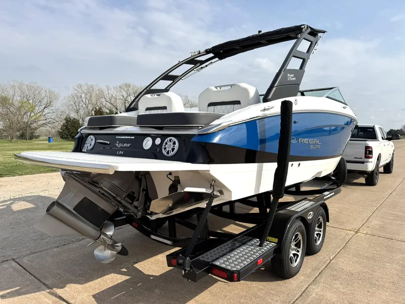 Slide: The Image of 2025 Regal LS4 Surf boat on trailer, blue and white design, parked outdoors. - 9