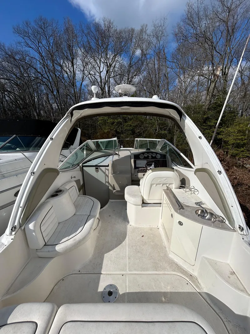 Slide: The Image of 2006 Sea Ray 290 Sundancer boat interior with seating and helm, surrounded by trees. - 2