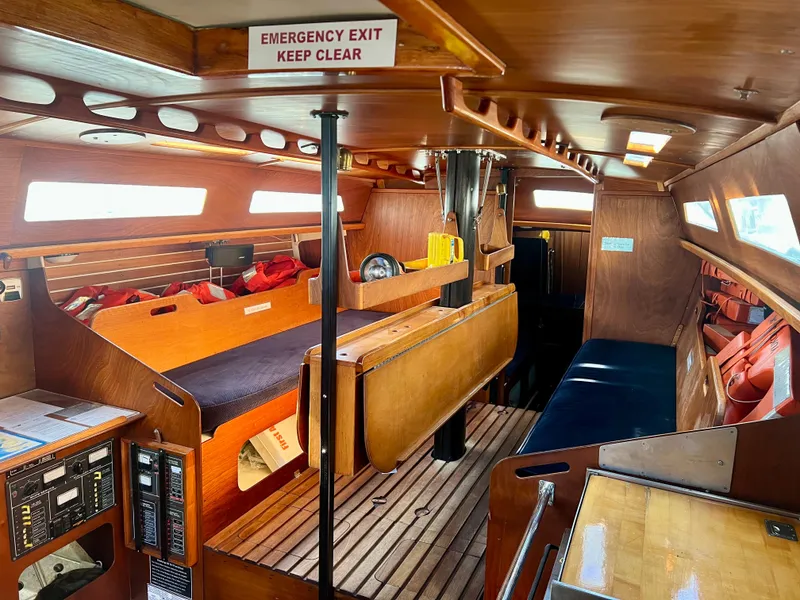 Slide: The Image of Interior of a 1985 Santa Cruz 50 sailboat, featuring wooden furnishings and emergency exit sign. - 22