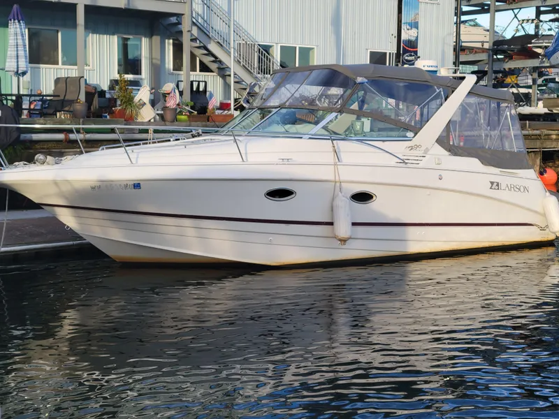 Slide: The Image of 1997 Larson 290 CABRIO boat docked at marina, white exterior, clear canopy. - 11