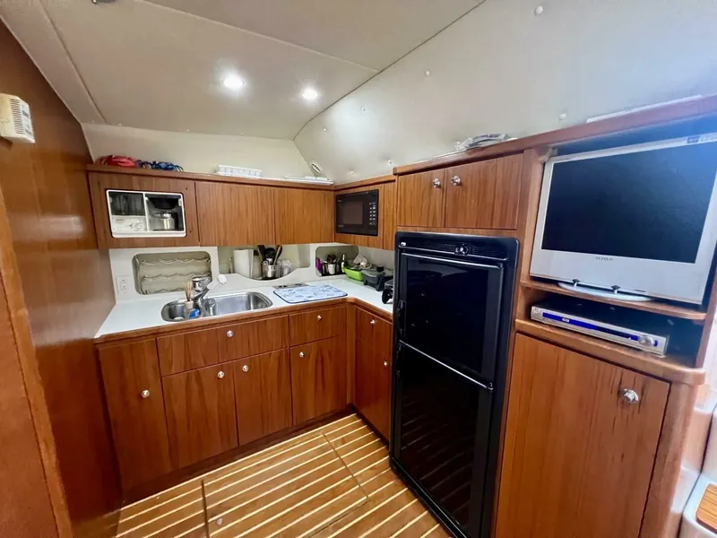 Slide: The Image of Interior of 1997 Tiara Yachts 41, featuring a compact kitchen with wood cabinetry and appliances. - 10