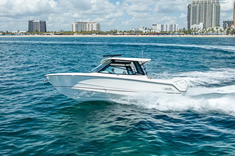 The Image of 2025 Boston Whaler 330 Vantage cruising on blue ocean near city skyline. - 0
