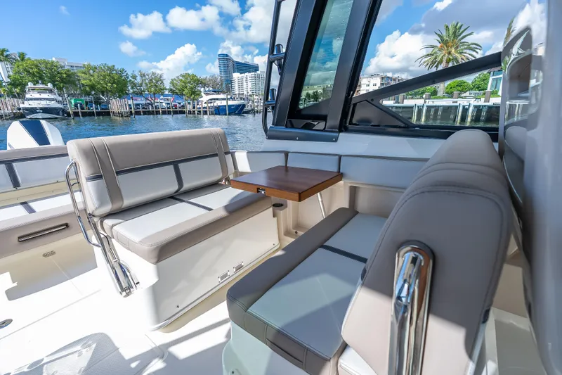 Slide: The Image of 2025 Boston Whaler 330 Vantage interior with seating and table, docked by waterfront. - 18