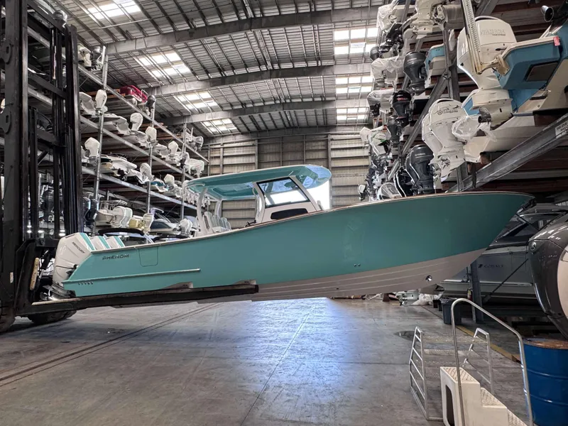 Slide: The Image of 2025 Phenom 37 CC boat in storage facility, turquoise hull, elevated by forklift. - 5