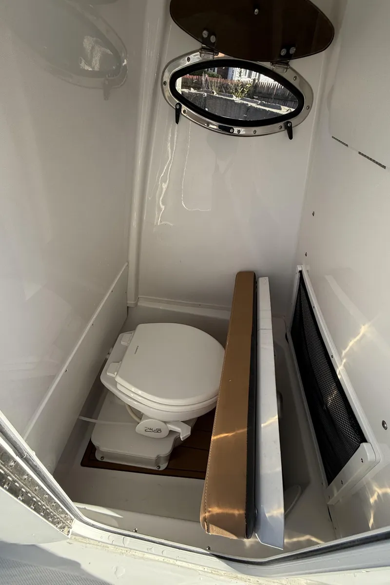 Slide: The Image of 2025 NauticStar 242OS boat interior with compact marine toilet and porthole. - 15