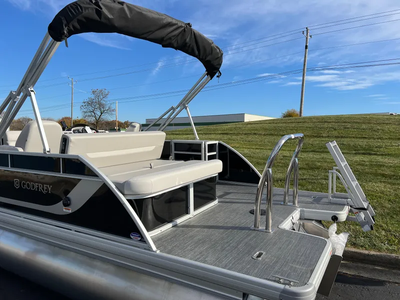 Slide: The Image of 2025 Godfrey XPERIENCE 2286 SFLC pontoon boat with seating and ladder, parked outdoors. - 6
