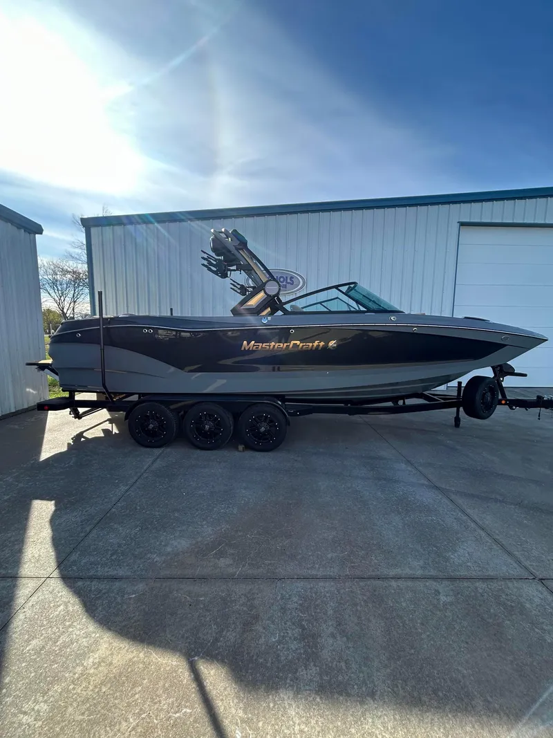 Slide: The Image of 2025 MasterCraft X26 boat on trailer, parked outside a garage. - 1