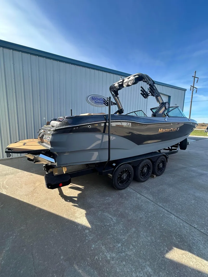 Slide: The Image of 2025 MasterCraft X26 boat on trailer, parked outside a building. - 2