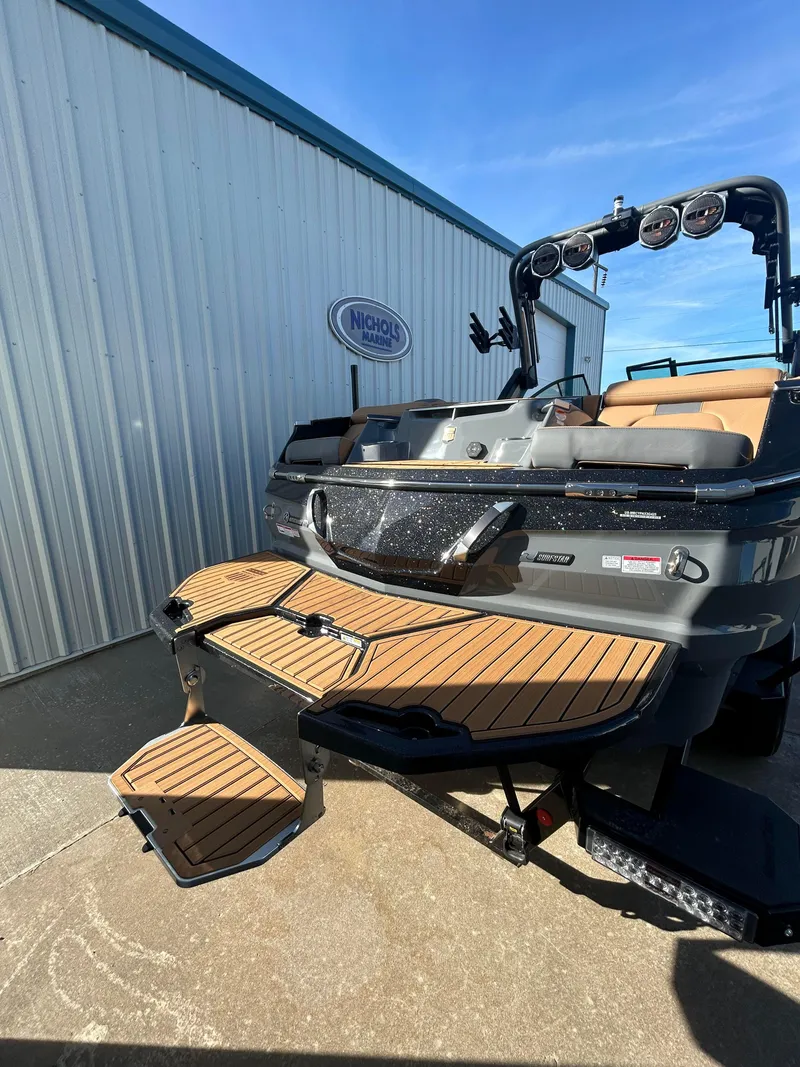 Slide: The Image of 2025 MasterCraft X26 boat with teak swim platform, docked near a metal building. - 4