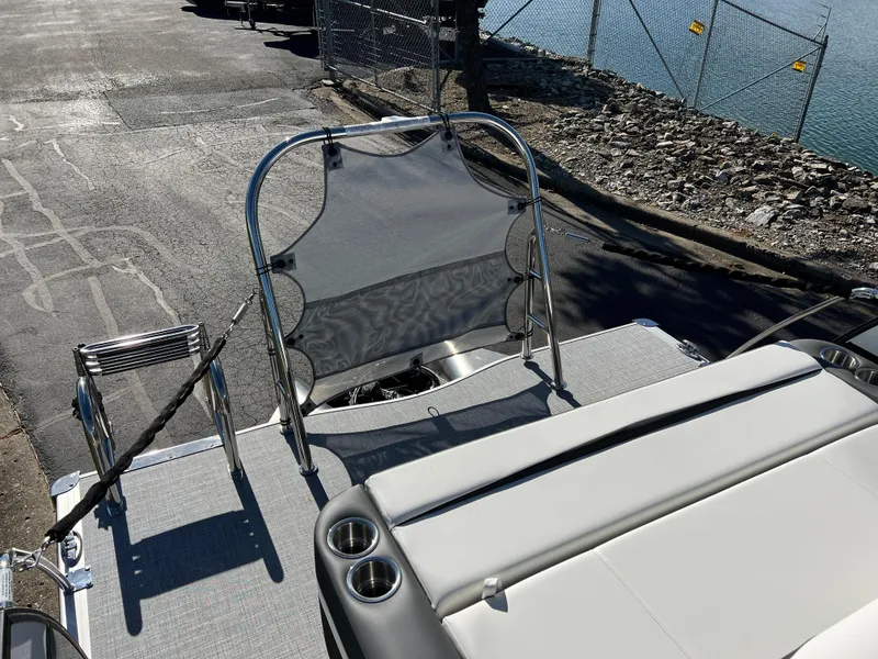Slide: The Image of 2025 South Bay S 224 UL pontoon boat with seating and cup holders, docked by a rocky shoreline. - 17