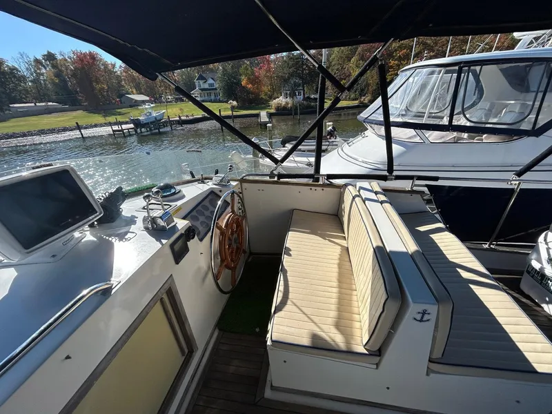 Slide: The Image of 1986 Grand Banks 42 Classic yacht interior with helm and seating, docked by a scenic waterfront. - 13