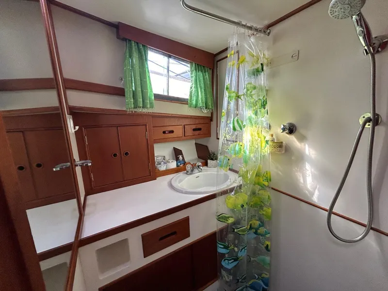 Slide: The Image of 1986 Grand Banks 42 Classic bathroom with wooden cabinets, green curtains, and a floral shower curtain. - 47