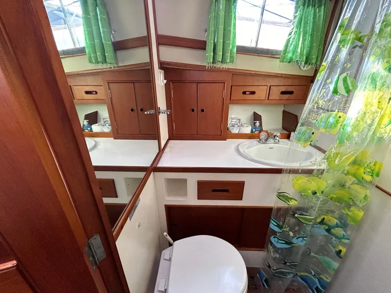 Slide: The Image of 1986 Grand Banks 42 Classic bathroom with wooden cabinets and fish-themed shower curtain. - 48